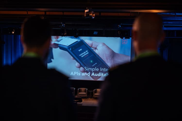 Two attendees in silhouette watching a conference screen showing ZAR ID identity validation on a handheld device